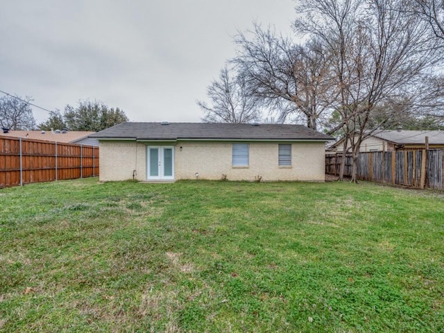 back of property with french doors, a fenced backyard, a yard, and brick siding