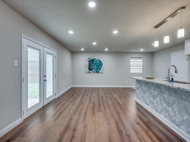 kitchen with a sink, baseboards, light stone counters, and wood finished floors