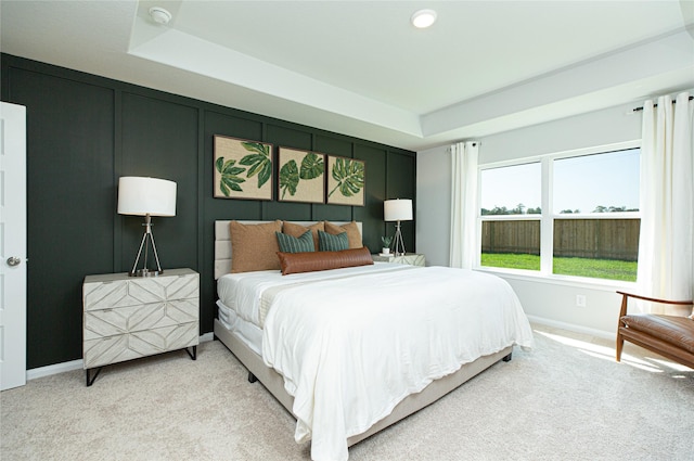 bedroom with carpet floors, a raised ceiling, a decorative wall, and baseboards