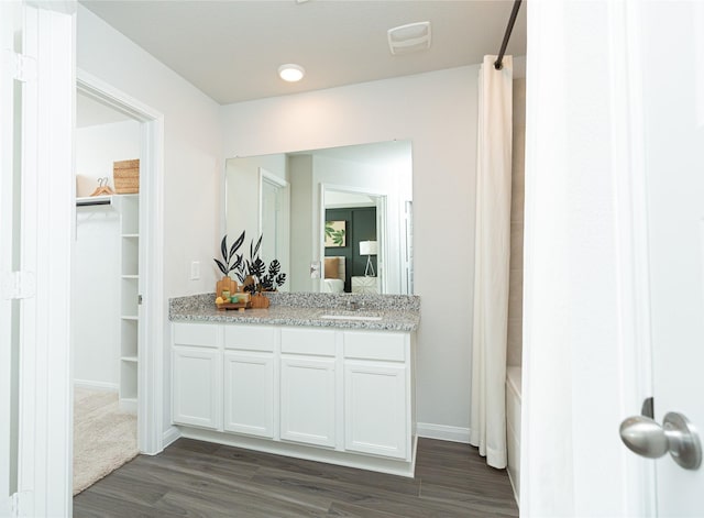 bathroom featuring wood finished floors, vanity, baseboards, a spacious closet, and shower / bath combo with shower curtain