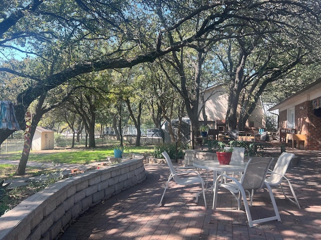 view of patio / terrace featuring an outbuilding, outdoor dining area, fence, and a storage unit