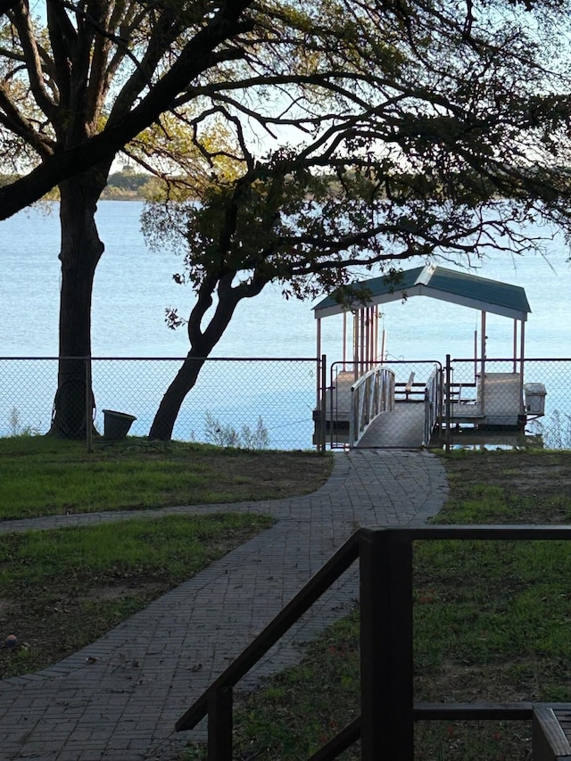 view of dock featuring a yard, a water view, and fence