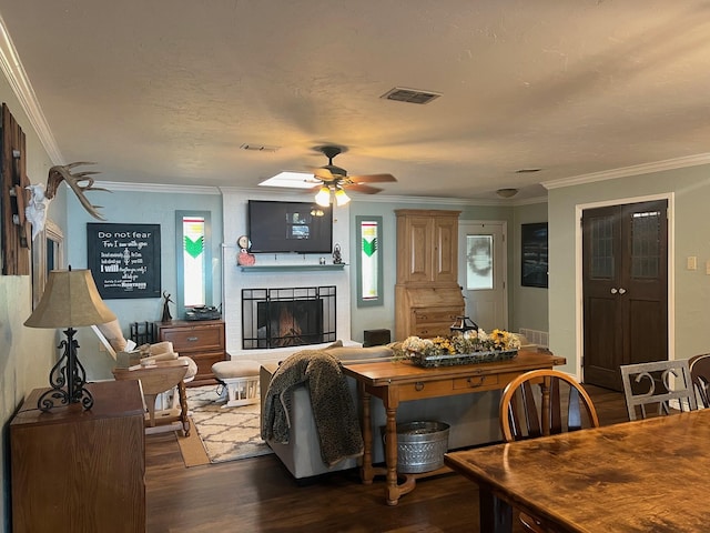 living area featuring ceiling fan, a fireplace, visible vents, ornamental molding, and dark wood finished floors