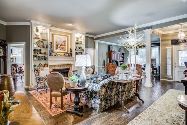 living room featuring a fireplace, wood finished floors, ornamental molding, ornate columns, and an inviting chandelier