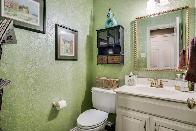 half bath with a textured wall, vanity, and toilet