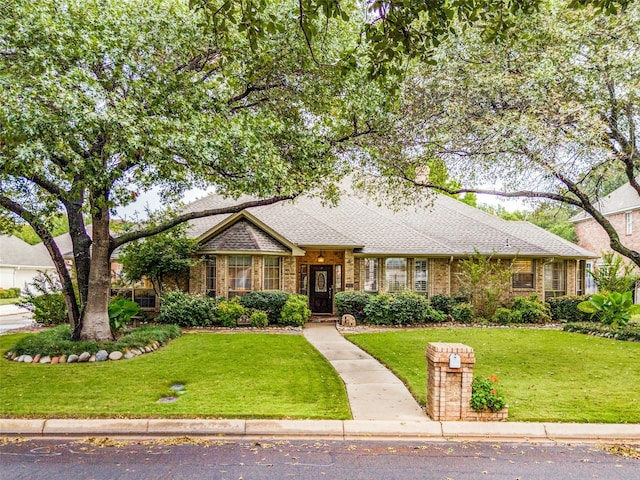 single story home featuring a shingled roof, a front lawn, and brick siding