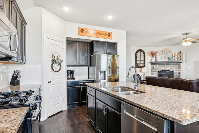 kitchen featuring dark wood finished floors, appliances with stainless steel finishes, open floor plan, a stone fireplace, and a sink