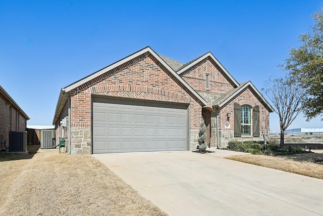 view of front of property with driveway, stone siding, an attached garage, cooling unit, and brick siding