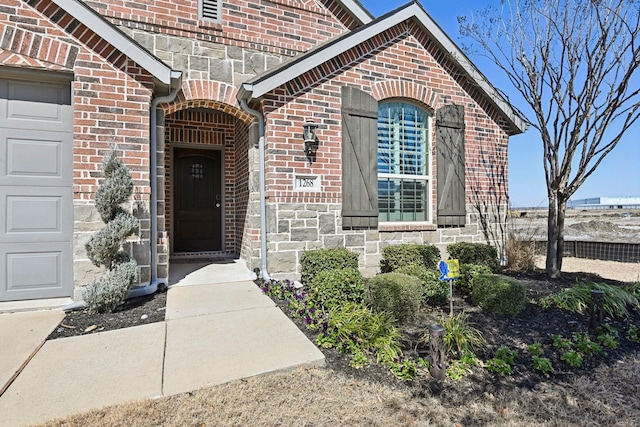 entrance to property with a garage, stone siding, and brick siding