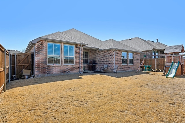 rear view of house featuring a shingled roof, a lawn, a fenced backyard, a playground, and brick siding