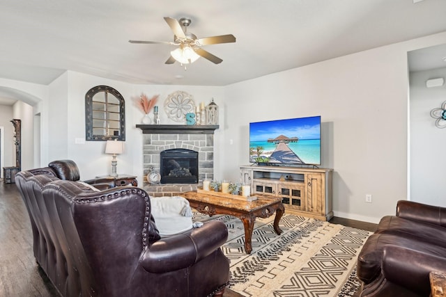 living room with baseboards, arched walkways, ceiling fan, wood finished floors, and a stone fireplace