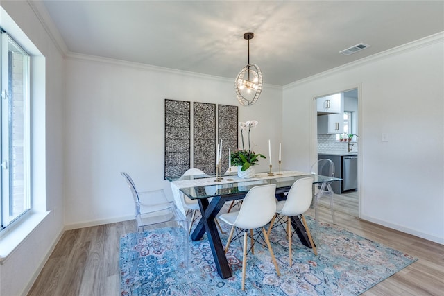 dining area featuring a chandelier, light wood-style flooring, visible vents, baseboards, and crown molding