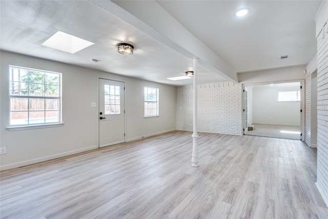 foyer with a skylight, brick wall, baseboards, and light wood-style floors