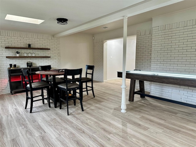 dining space with brick wall, light wood finished floors, and a skylight