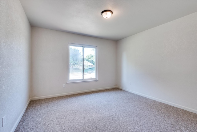 spare room with carpet floors, a textured wall, and baseboards