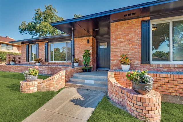 property entrance with a yard, a porch, and brick siding