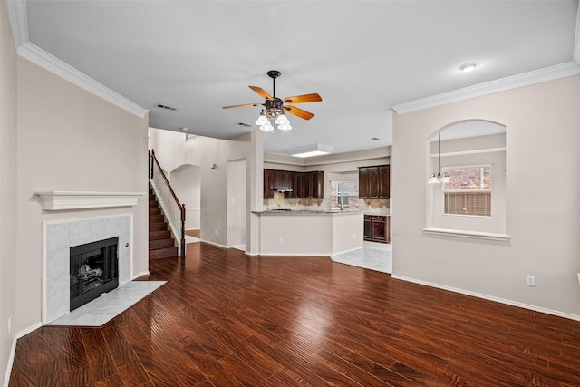 unfurnished living room with ornamental molding, a tile fireplace, wood finished floors, and visible vents