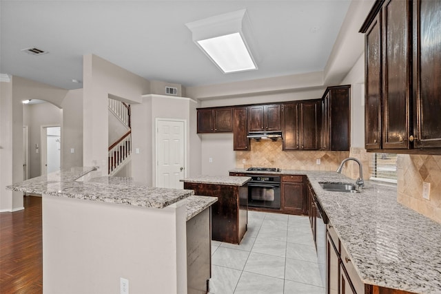 kitchen with under cabinet range hood, a kitchen island, a sink, visible vents, and black oven