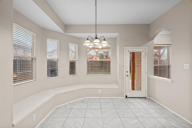 unfurnished dining area featuring baseboards, light tile patterned floors, arched walkways, and an inviting chandelier