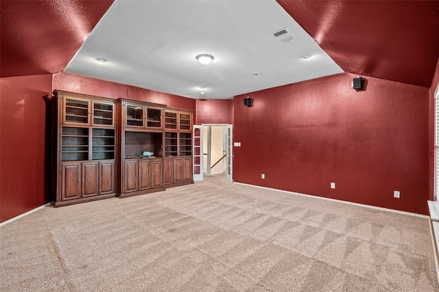 empty room with lofted ceiling, a textured wall, light carpet, visible vents, and baseboards