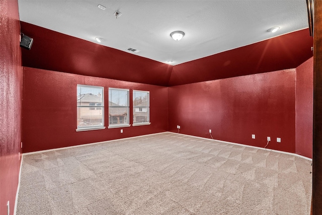 unfurnished room with carpet floors, a textured wall, visible vents, and vaulted ceiling