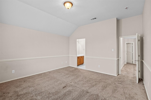 unfurnished bedroom with light carpet, baseboards, visible vents, lofted ceiling, and ensuite bathroom