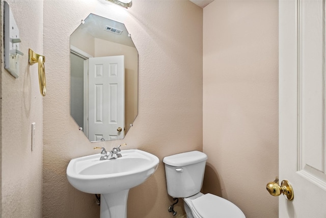 half bathroom with toilet, visible vents, a sink, and a textured wall