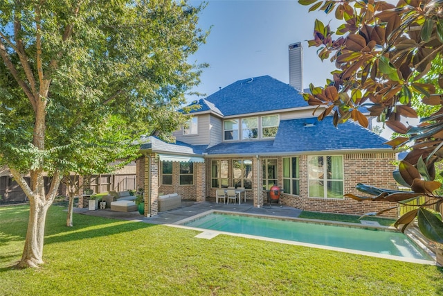 rear view of property featuring brick siding, a shingled roof, a lawn, a chimney, and a patio area