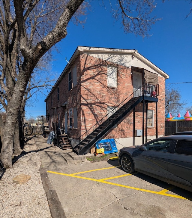 exterior space with uncovered parking, brick siding, stairway, and fence