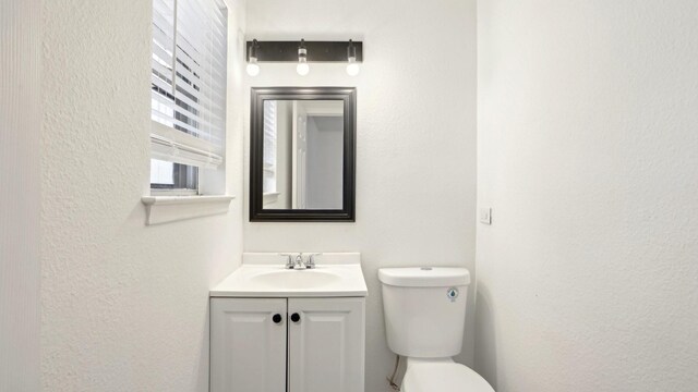 half bathroom with toilet, a textured wall, and vanity