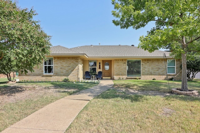 single story home featuring a shingled roof, brick siding, and a front lawn