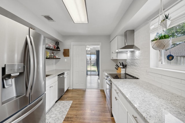 kitchen featuring light stone counters, dark wood-style floors, stainless steel appliances, tasteful backsplash, and wall chimney range hood