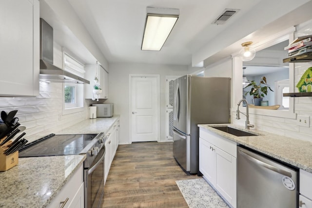 kitchen featuring visible vents, appliances with stainless steel finishes, white cabinets, a sink, and wall chimney range hood