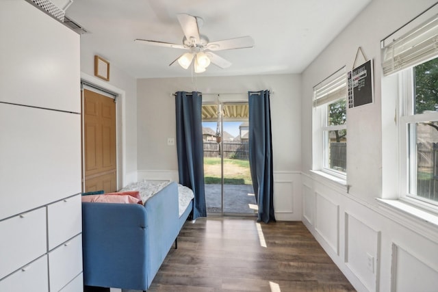 doorway with dark wood-type flooring, a wainscoted wall, a decorative wall, and ceiling fan