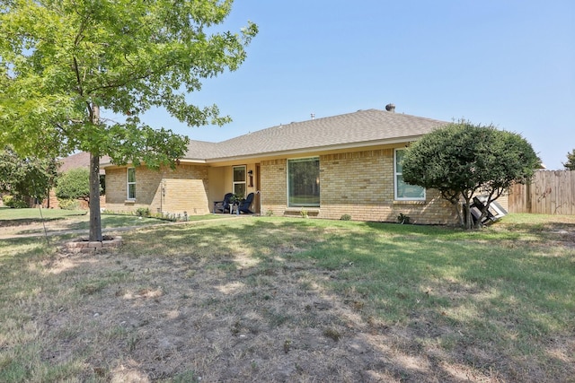 back of house featuring a yard, brick siding, roof with shingles, and fence