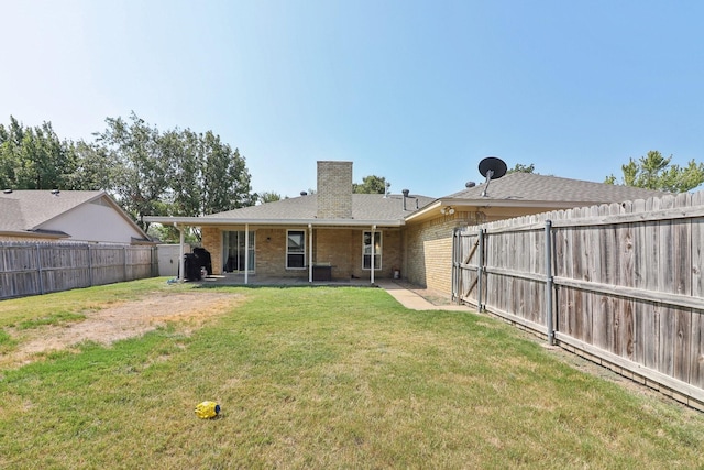 rear view of house with a lawn, a patio, a fenced backyard, a chimney, and brick siding