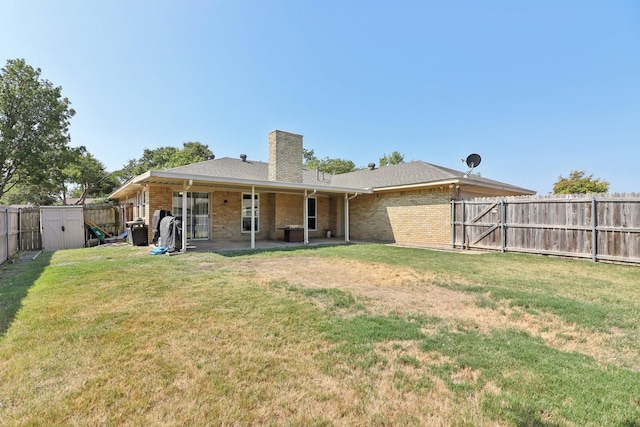 rear view of house with brick siding, a fenced backyard, a chimney, and a yard