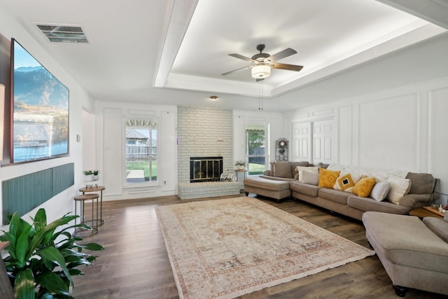 living area with plenty of natural light, a raised ceiling, visible vents, and a decorative wall