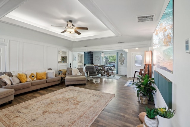 living room featuring a decorative wall, a ceiling fan, visible vents, a tray ceiling, and dark wood finished floors