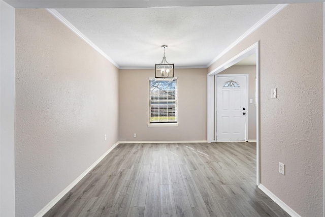 unfurnished dining area with wood finished floors, baseboards, a textured wall, and ornamental molding