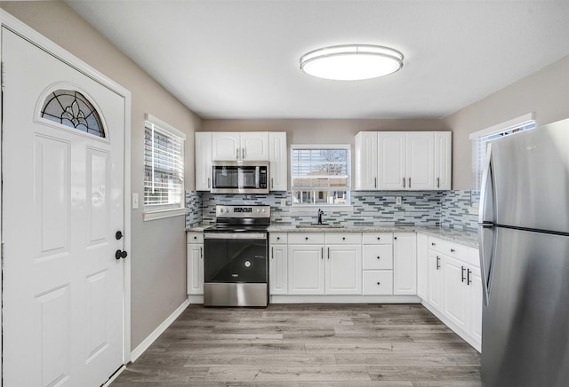 kitchen with decorative backsplash, light wood-type flooring, appliances with stainless steel finishes, and a sink