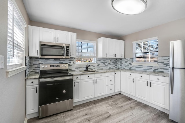 kitchen featuring light wood-style flooring, a sink, stainless steel appliances, white cabinets, and tasteful backsplash