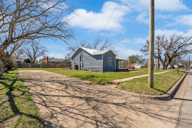 view of home's exterior with a lawn, driveway, metal roof, and fence