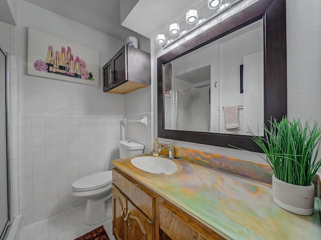 bathroom featuring toilet, vanity, tile walls, and a shower with shower door