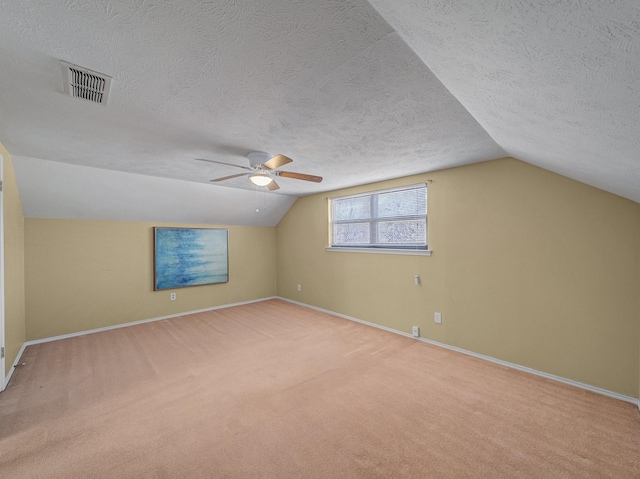 bonus room with a textured ceiling, lofted ceiling, light colored carpet, visible vents, and baseboards