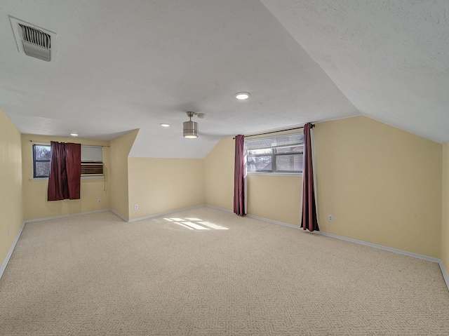 additional living space featuring a textured ceiling, carpet flooring, visible vents, baseboards, and vaulted ceiling