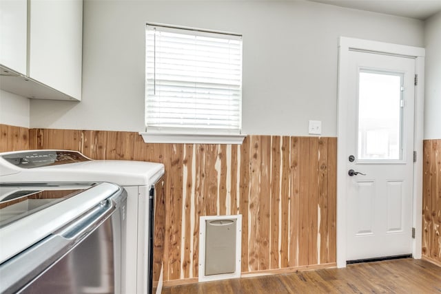 clothes washing area featuring cabinet space, wooden walls, separate washer and dryer, and a wainscoted wall