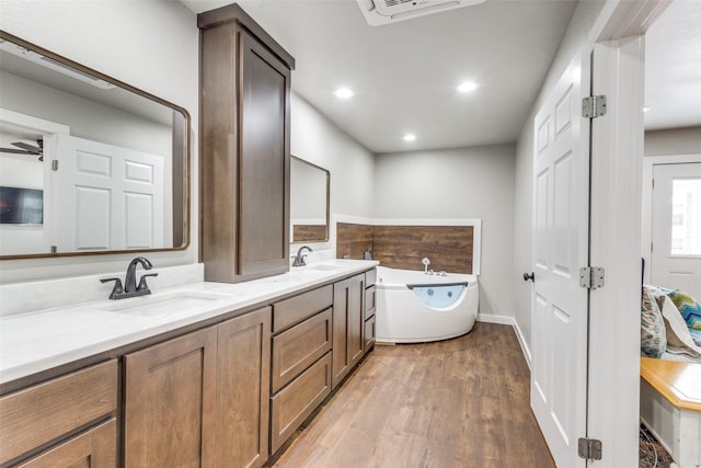 bathroom with double vanity, a washtub, a sink, and wood finished floors