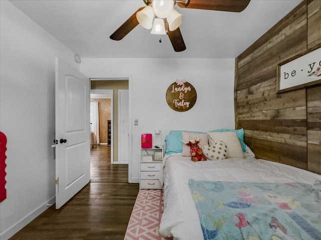 bedroom with baseboards, wooden walls, a ceiling fan, and wood finished floors