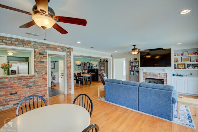 living room with brick wall, light wood-style flooring, a brick fireplace, and visible vents